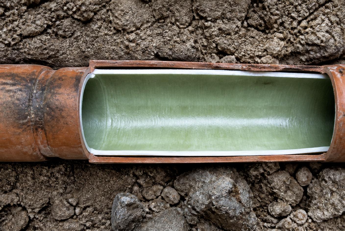 Cutaway of an underground clay drain pipe with a cured resin liner forming a smooth new inner wall